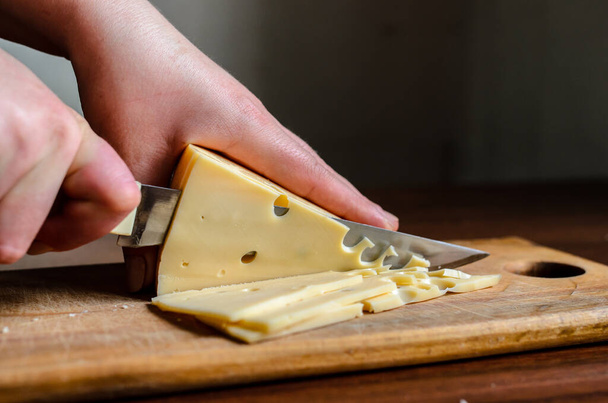 Slicing cheese on a wooden board. - Fotoğraf, Görsel