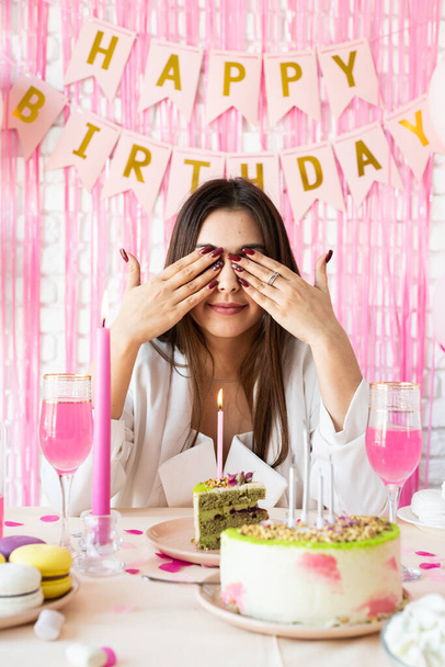 Geburtstagsfeier. Geburtstagstische. Attraktive brünette Frau in weißer Partykleidung bereitet Geburtstagstisch mit Kuchen, Cakepops, Macarons und anderen Süßigkeiten und macht Wünsche - Foto, Bild