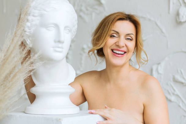 Schöne Frau mit sauberer Haut und nackten Schultern, die neben einer antiken Gips-Skulptur posiert. Weibliche Schönheit und Reinheit - Foto, Bild