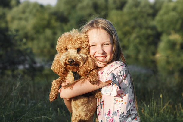 Pudelhund und sein Herrchen. Liebenswerter Welpe und kleines Mädchen umarmen sich und haben Spaß im Park, Kopierraum - Foto, Bild