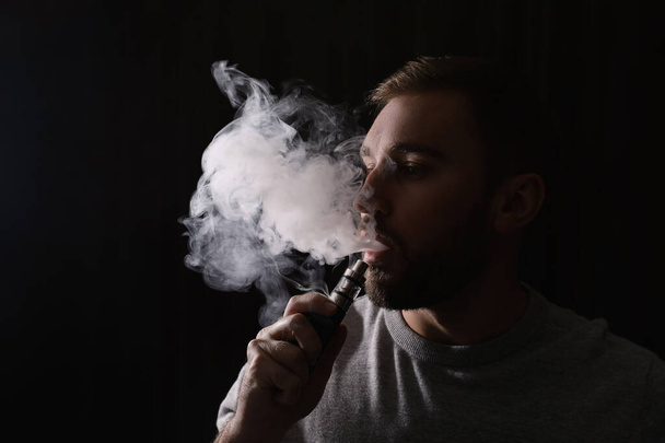 Man using electronic cigarette on black background - Foto, afbeelding