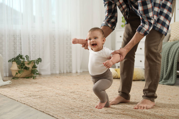 Father supporting his baby daughter while she learning to walk at home - Φωτογραφία, εικόνα