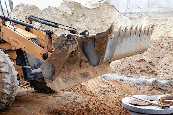 La excavadora llena la fosa con el cubo delantero. Mueve el suelo alrededor del sitio de construcción. Primer plano. Equipos de construcción pesados - Foto, Imagen