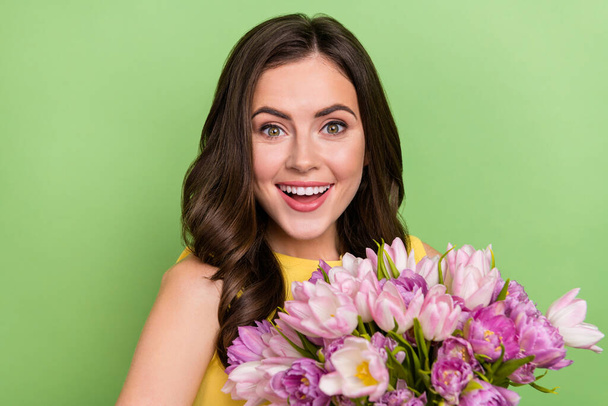 Portrait of attractive cheerful wavy-haired girl holding flowers having fun isolated over bright green color background - Photo, Image