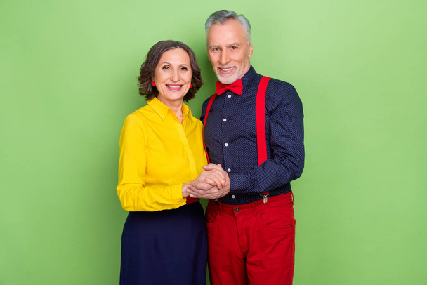 Photo of two peaceful friendly pensioners hold arms enjoy 60s discotheque isolated on green color background - Foto, afbeelding