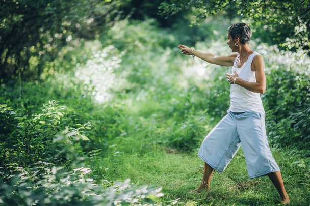 自然とのバランスで-自然の中でエネルギーを与え、受信する心の練習。緑豊かな森の中で瞑想を練習女性,サイドビュー - 写真・画像