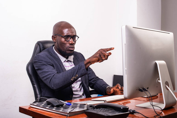 młody biznesmen noszący okulary optyczne siedzący przy biurku i wskazujący palcem na ekran laptopa. - Zdjęcie, obraz