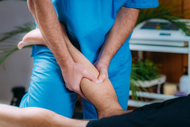 Fizyoterapist, yaralı baldırıyla erkek hastaya masaj yapıyor. Spor sakatlığı tedavisi. - Fotoğraf, Görsel