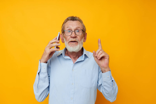 Photo of retired old man gray beard with glasses talking on the phone yellow background - Foto, afbeelding