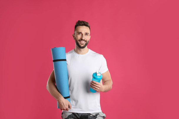 Handsome man with yoga mat and shaker on pink background - Foto, immagini