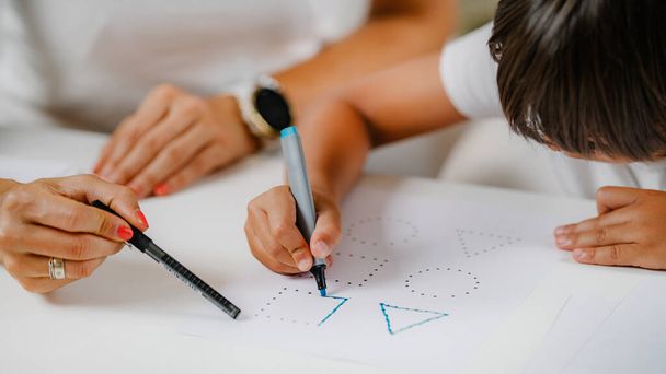 Child drawing shapes in a preschooler assessment test. Psychologist helping him. - Фото, зображення