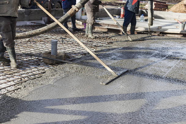 İnşaat işçisi endüstriyel bir atölyede beton döşemeyi yıkıyor. Bacakları betonun içinde. Yüzey somutlaşıyor. Monolitik güçlendirilmiş beton çalışmalar - Fotoğraf, Görsel