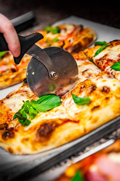 chef hand with cutter cutting pizza to pieces at pizzeria - Foto, immagini
