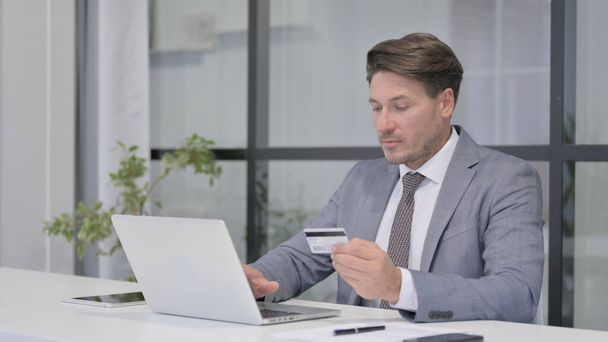 Чоловік середнього віку робить онлайн платежі на ноутбуці в офісі
 - Фото, зображення