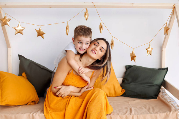 Young happy family loving mother and her child son having fun together at home, playing and laughing. Smiling kid hugging embracing his mom, happy to spend leisure time on weekend with mommy - Φωτογραφία, εικόνα