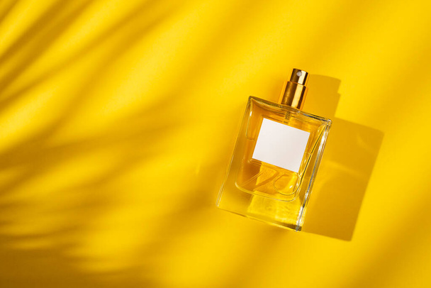 Transparante fles parfum met etiket op gele achtergrond. Parfumpresentatie met daglicht. Trending concept in natuurlijke materialen met mooie schaduw. De essentie van vrouwen. - Foto, afbeelding