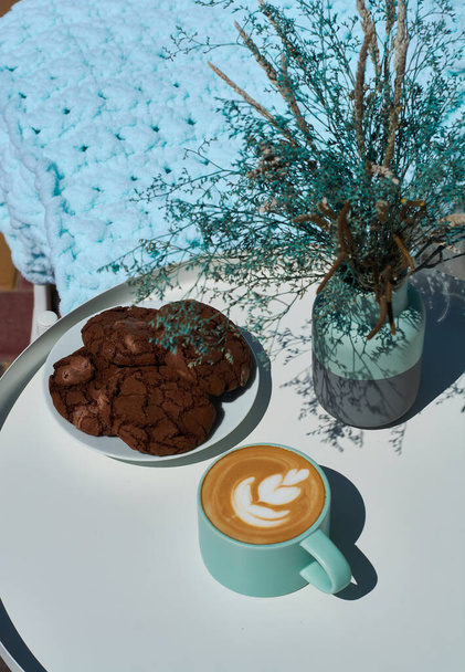 朝のカプチーノは夏のテラスのコーヒーショップで花とチョコレートクッキー. - 写真・画像