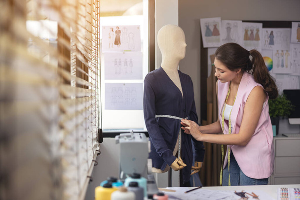 An ihrem Arbeitsplatz modifiziert eine asiatische Schneiderin das Design eines Kleidungsstücks an einer Schaufensterpuppe. - Foto, Bild