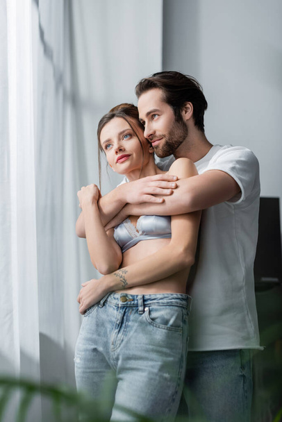 pleased bearded man hugging tattooed girlfriend in bra - Фото, зображення