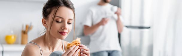 young woman holding croissant near blurred man on background, banner - Foto, Imagem