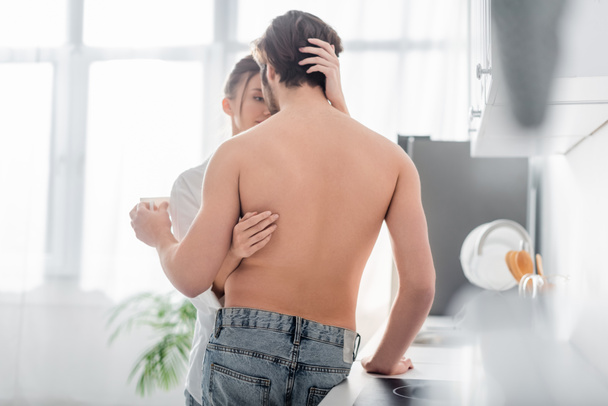 back view of shirtless man holding cup and hugging with sensual woman  - Photo, Image