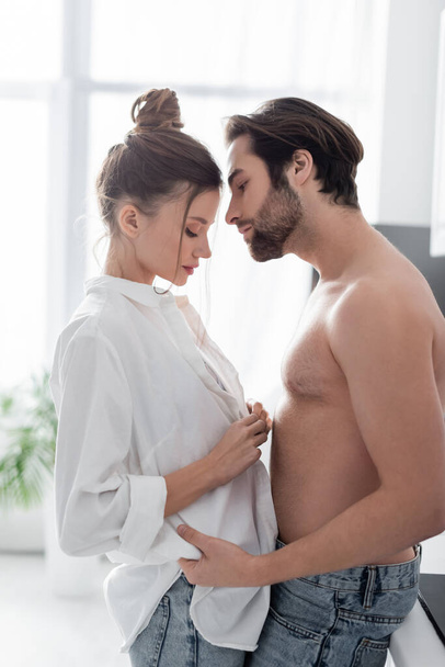 side view of young woman unbuttoning shirt near muscular man  - Foto, afbeelding