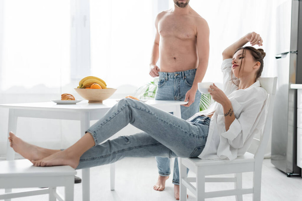 homme barbu en jeans debout près de la jeune femme avec tatouage dans la cuisine  - Photo, image