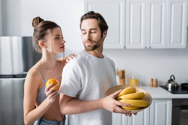 jeune femme en soutien-gorge tenant orange près de l'homme avec des bananes - Photo, image