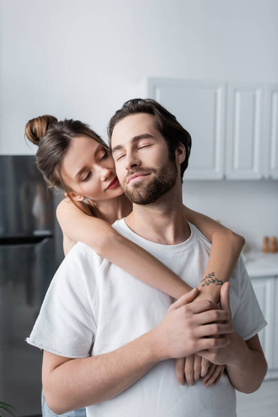 mujer joven tatuada abrazando a hombre barbudo en camiseta blanca - Foto, imagen