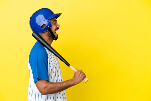 Young Colombian latin man playing baseball isolated on yellow background laughing in lateral position - Photo, Image