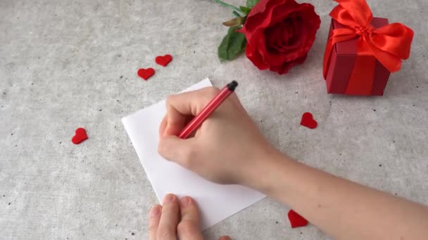 La donna disegna un cuore per la celebrazione del 14 febbraio. Cuori, rosa e scatola regalo rossa sul tavolo - Filmati, video