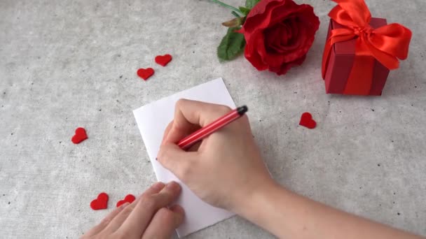 Жінка пише масаж до святкування 14 лютого. Серця, троянда і червона скринька з подарунками на столі. - Кадри, відео
