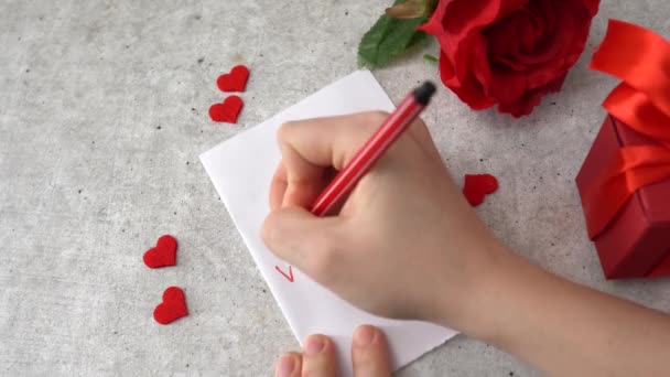 Mujer escribe masaje Te amo para 14 Febrero celebración. Corazones, rosa y caja de regalo roja en la mesa - Imágenes, Vídeo