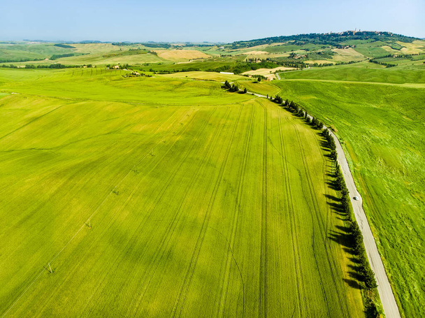 Stunning aerial view of green fields and farmlands with small villages on the horizon. Summer rural landscape of rolling hills, curved roads and cypresses of Tuscany, Italy. - Foto, afbeelding