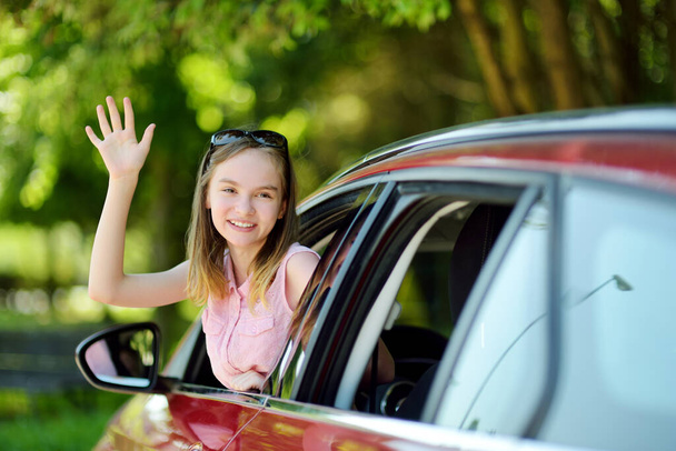 Funny young girl sticking her head out the car window looking forward for a roadtrip or travel. Family car travel with kids. - Zdjęcie, obraz