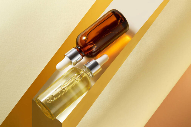 Komposition aus braunen und transparenten Glasflaschen mit aromatischen natürlichen ätherischen Ölen. Kosmetikprodukte auf gelbem geometrischen Hintergrund. Alternative Medizin, natürliche Therapie.  - Foto, Bild