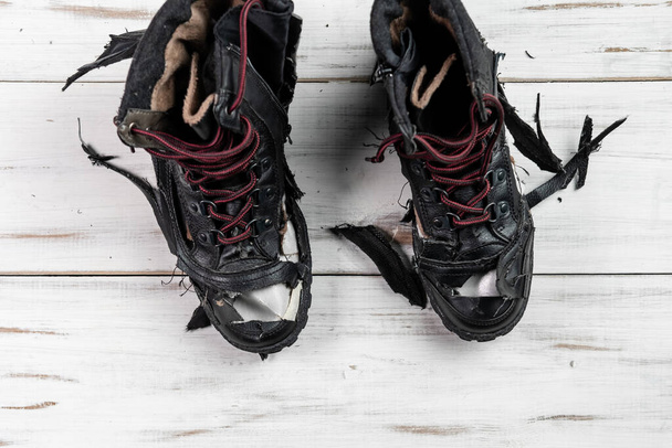 Torn worn shoes boots. Light wooden background. Torn, broken shoes. - Фото, изображение