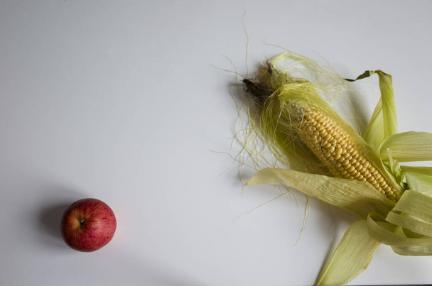 Sweet corn cob and red apple flat lay on white table. Homegrown real organic vegetable and fruit not perfect look. Selective short focus Natural light, space for text. Autumn harvest background - Foto, immagini