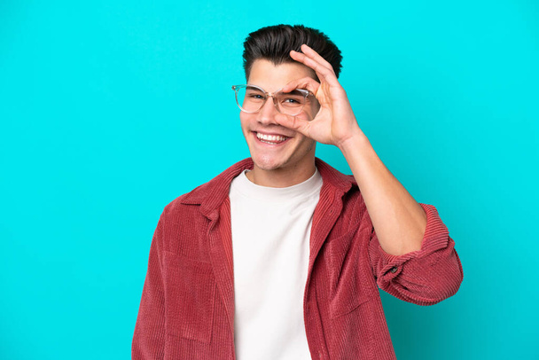 Молодий красивий кавказький чоловік ізольований на синьому пекарні З окулярами з щасливим виразом
 - Фото, зображення