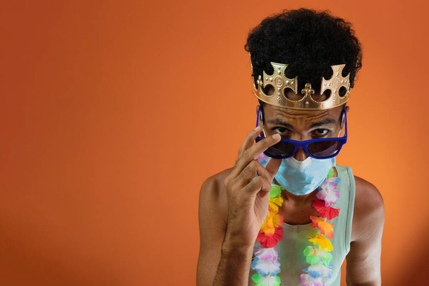 Černoch v kostýmu pro karneval s pandemickou maskou izolované na oranžovém pozadí.  - Fotografie, Obrázek
