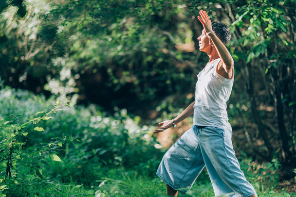 In balance with nature - Mindful practice of giving and receiving energy through nature. Woman practicing meditation in the lush green forest, side view - Foto, Imagem