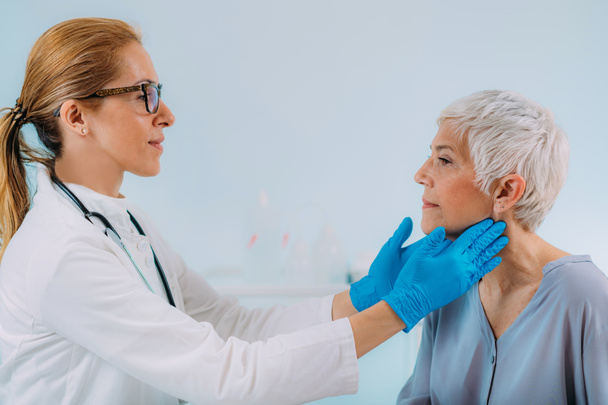 Endocrinology doctor examining a senior woman with thyroid gland disease symptoms - Foto, imagen