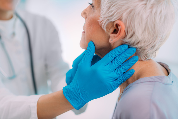 Ενδοκρινολογικός γιατρός εξετάζει μια ηλικιωμένη γυναίκα με συμπτώματα νόσου του θυρεοειδούς αδένα - Φωτογραφία, εικόνα