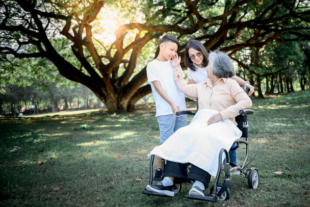 Азиатская пожилая женщина сидит в инвалидной коляске, улыбается и счастлив с дочерью и внуком заботиться о ней, к отношениям азиатской семьи и пенсионного возраста. - Фото, изображение