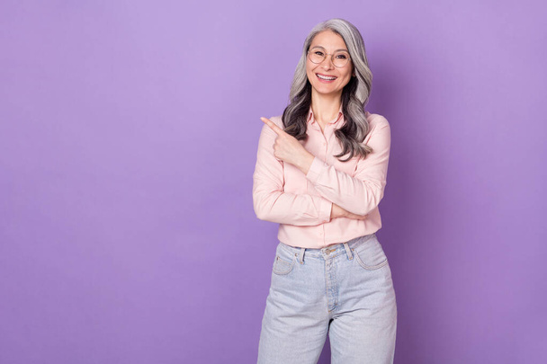 Portrait of attractive trendy elderly retired cheerful businesswoman demonstrating copy space ad isolated over violet purple color background - Zdjęcie, obraz