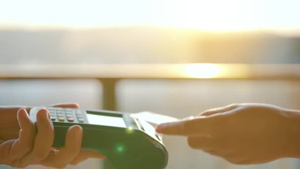 NFC luottokorttimaksu. Nainen maksaa kontaktittomalla luottokortilla NFC-teknologialla. Langaton rahansiirto. Kortti kone miehen kädessä auringonvalossa tausta - Materiaali, video