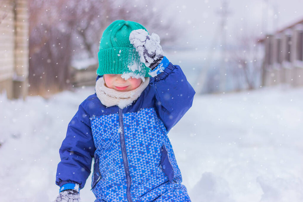 child boy in warm winter clothes playing snowballs on a snowy street. winter holidays, outdoor activities in the snow, childhood. - Photo, Image