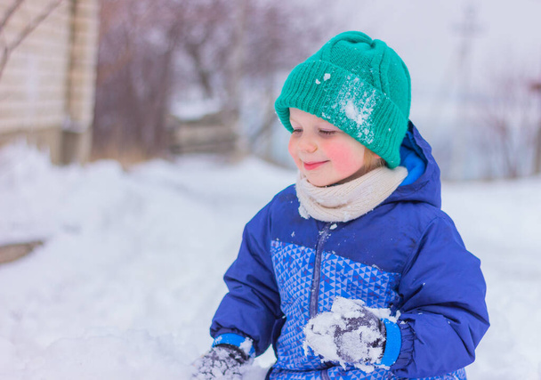verspielter Junge in warmer Winterkleidung, der auf einer verschneiten Straße Schneebälle spielt. Winterurlaub, Outdoor-Aktivitäten im Schnee, Kindheit. - Foto, Bild