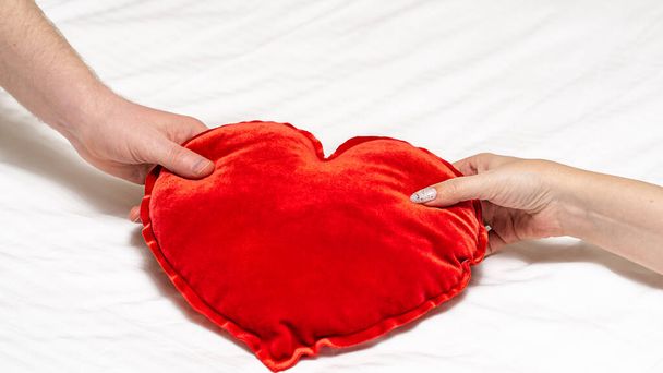 Τα θηλυκά και τα αρσενικά χέρια κρατούν το κόκκινο μαξιλάρι της καρδιάς μαζί. Ημέρα του Αγίου Βαλεντίνου - Φωτογραφία, εικόνα
