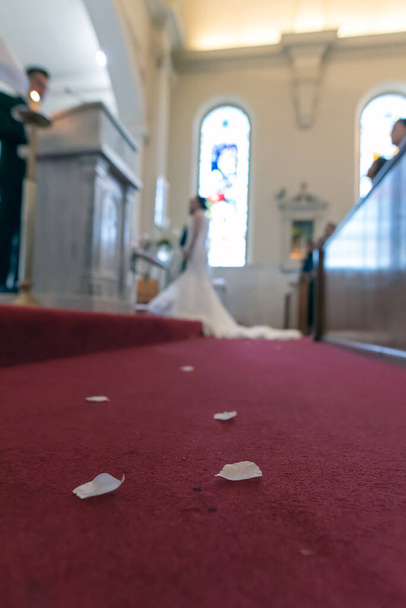 Rosenblätter verstreut auf dem Fußboden der katholischen Kirche führen hinauf zum beleuchteten Altar mit Braut und Bräutigam. - Foto, Bild